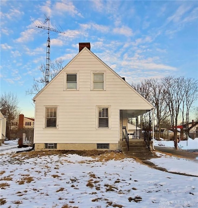 snow covered rear of property with a porch and a chimney