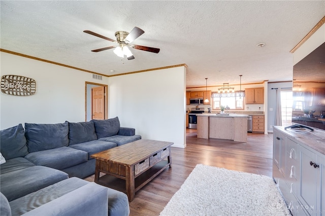 living room with visible vents, ornamental molding, a ceiling fan, a textured ceiling, and light wood-type flooring