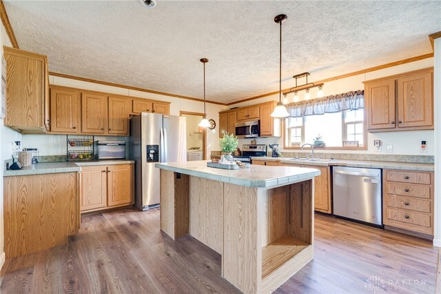 kitchen with appliances with stainless steel finishes, light wood-type flooring, a sink, and crown molding