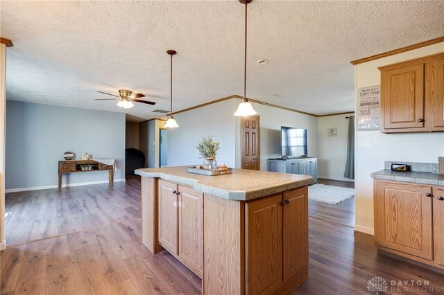 kitchen featuring a textured ceiling, a kitchen island, open floor plan, ornamental molding, and dark wood finished floors