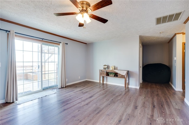 spare room with a textured ceiling, wood finished floors, visible vents, baseboards, and crown molding