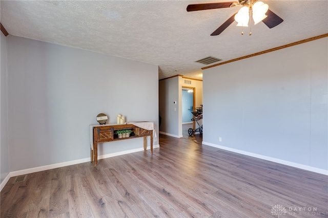 empty room featuring baseboards, visible vents, ornamental molding, wood finished floors, and a textured ceiling