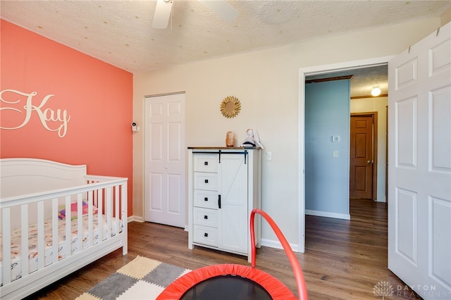 bedroom with a textured ceiling, wood finished floors, a ceiling fan, baseboards, and a nursery area