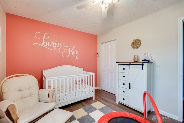 bedroom featuring a textured ceiling, ceiling fan, wood finished floors, baseboards, and a crib