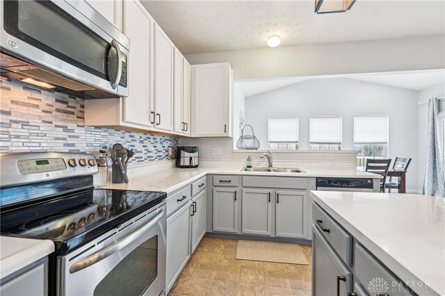 kitchen with appliances with stainless steel finishes, gray cabinets, a sink, and light countertops