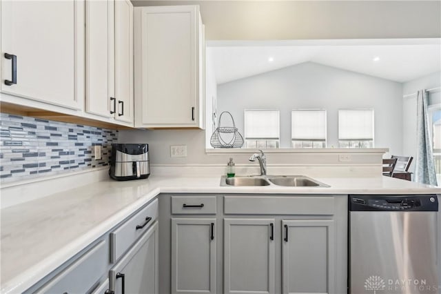 kitchen with lofted ceiling, a peninsula, a sink, light countertops, and dishwasher