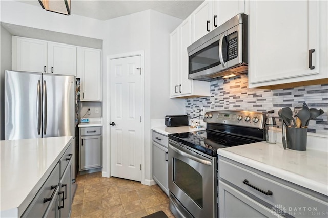 kitchen featuring light countertops, backsplash, gray cabinetry, appliances with stainless steel finishes, and white cabinetry