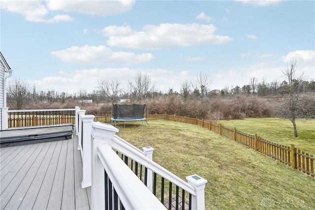 wooden deck with a trampoline, a fenced backyard, and a yard