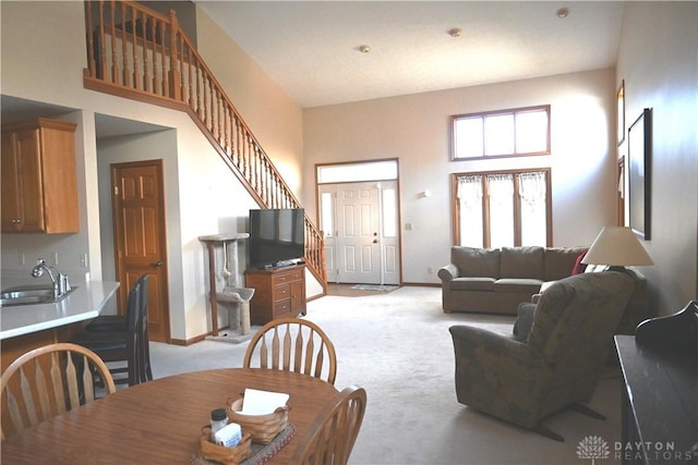 dining room featuring a towering ceiling, baseboards, stairway, and light colored carpet