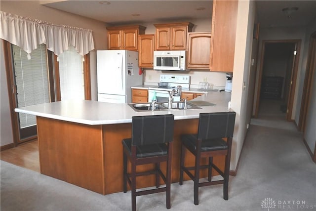 kitchen with a breakfast bar area, a peninsula, white appliances, light countertops, and brown cabinets