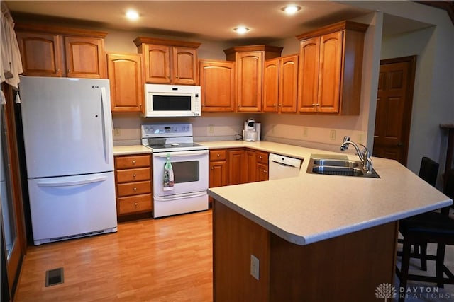 kitchen featuring white appliances, visible vents, a peninsula, a kitchen bar, and a sink