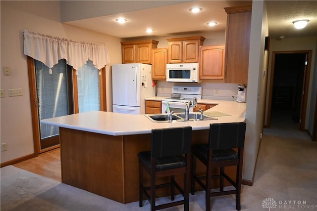 kitchen with white appliances, a breakfast bar, a peninsula, light countertops, and recessed lighting