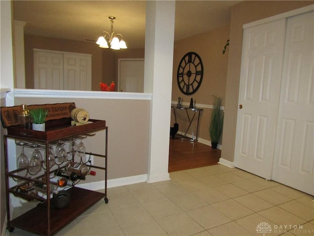 hallway featuring tile patterned flooring, baseboards, and a notable chandelier