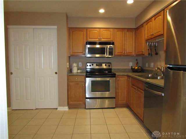 kitchen featuring light tile patterned floors, appliances with stainless steel finishes, brown cabinets, a sink, and recessed lighting