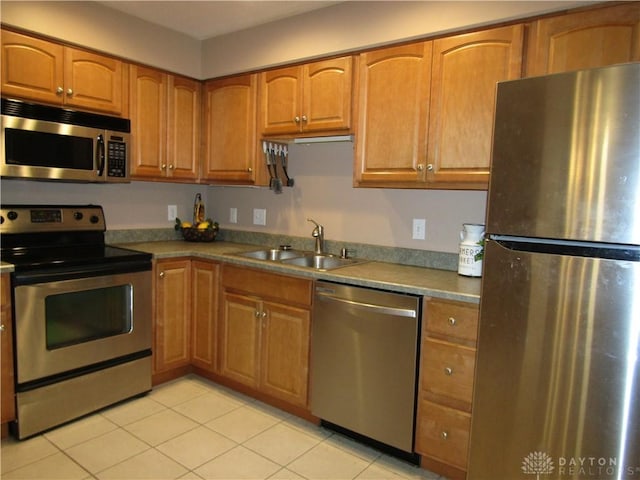 kitchen with appliances with stainless steel finishes, brown cabinetry, a sink, and light tile patterned floors