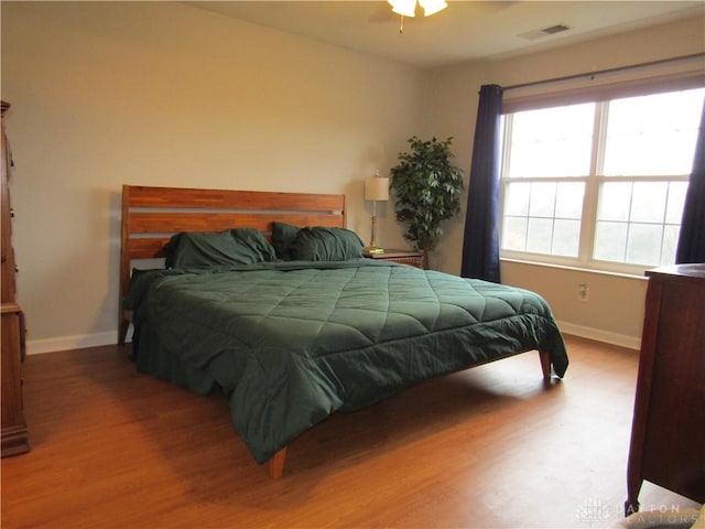 bedroom with wood finished floors, visible vents, and baseboards