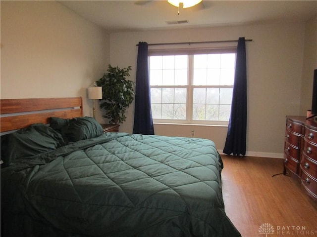 bedroom with a ceiling fan, visible vents, baseboards, and wood finished floors