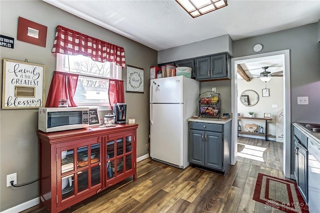 kitchen with dark wood-style floors, stainless steel microwave, freestanding refrigerator, and baseboards