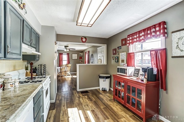 kitchen featuring a textured ceiling, under cabinet range hood, white appliances, a ceiling fan, and dark wood finished floors