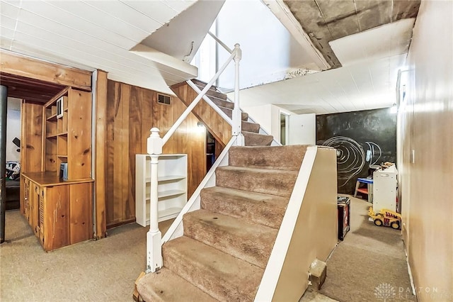 staircase featuring visible vents, wooden walls, and carpet flooring