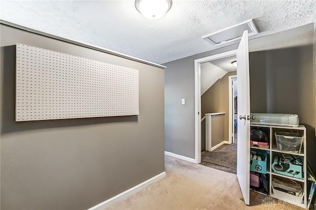 hall featuring carpet, attic access, baseboards, and a textured ceiling