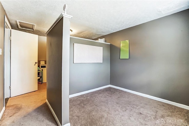 spare room featuring attic access, carpet flooring, a textured ceiling, and baseboards