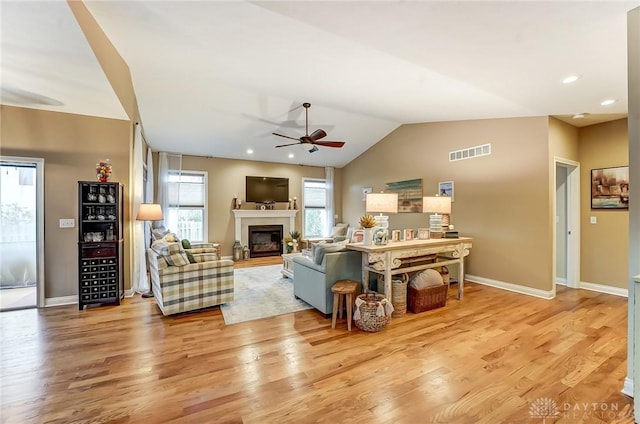 living room featuring lofted ceiling, visible vents, a glass covered fireplace, wood finished floors, and baseboards