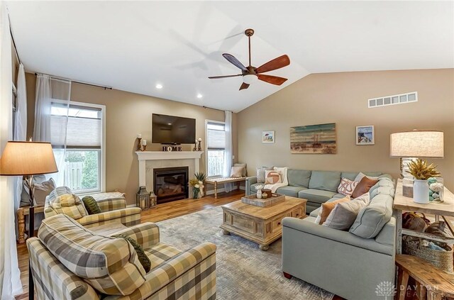 living room with visible vents, a glass covered fireplace, vaulted ceiling, ceiling fan, and wood finished floors