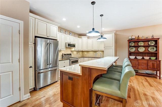 kitchen with light wood-type flooring, appliances with stainless steel finishes, backsplash, and decorative light fixtures