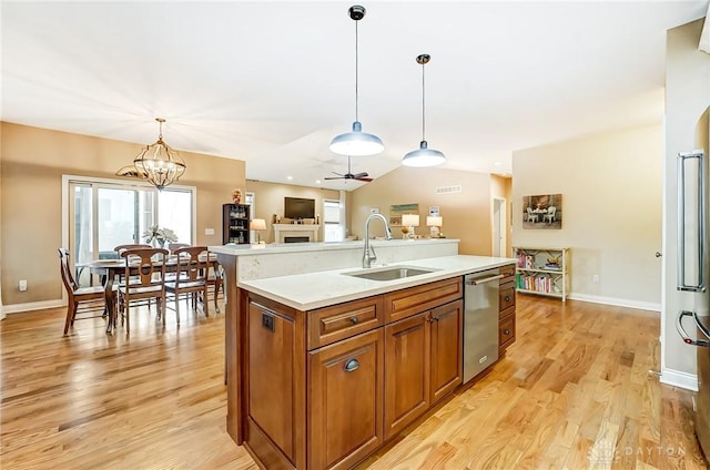 kitchen with light countertops, stainless steel dishwasher, brown cabinetry, a sink, and light wood-type flooring