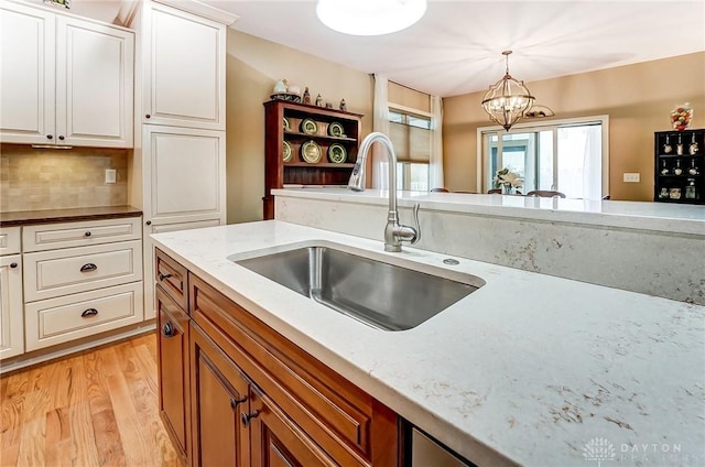 kitchen featuring light stone counters, decorative light fixtures, light wood-style floors, white cabinets, and a sink