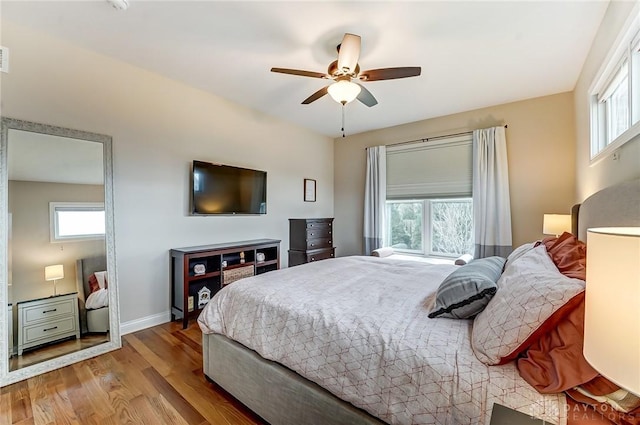 bedroom featuring multiple windows, ceiling fan, baseboards, and wood finished floors