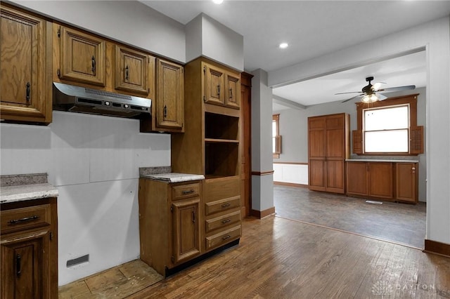 kitchen featuring ceiling fan, under cabinet range hood, wood finished floors, baseboards, and brown cabinetry