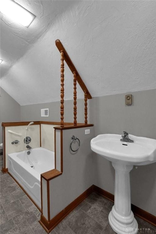 bathroom with a textured ceiling, lofted ceiling, visible vents, baseboards, and a bath