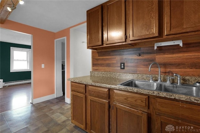 kitchen featuring tasteful backsplash, a baseboard heating unit, brown cabinetry, and a sink