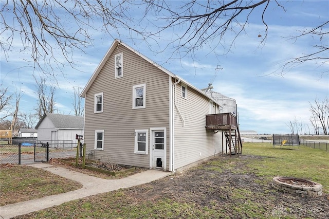 view of side of property with an outdoor fire pit, a trampoline, fence, and a gate