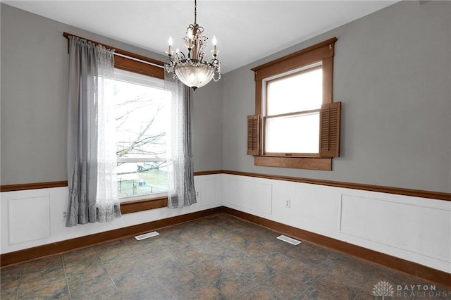 empty room featuring a chandelier, a wainscoted wall, visible vents, and stone finish flooring