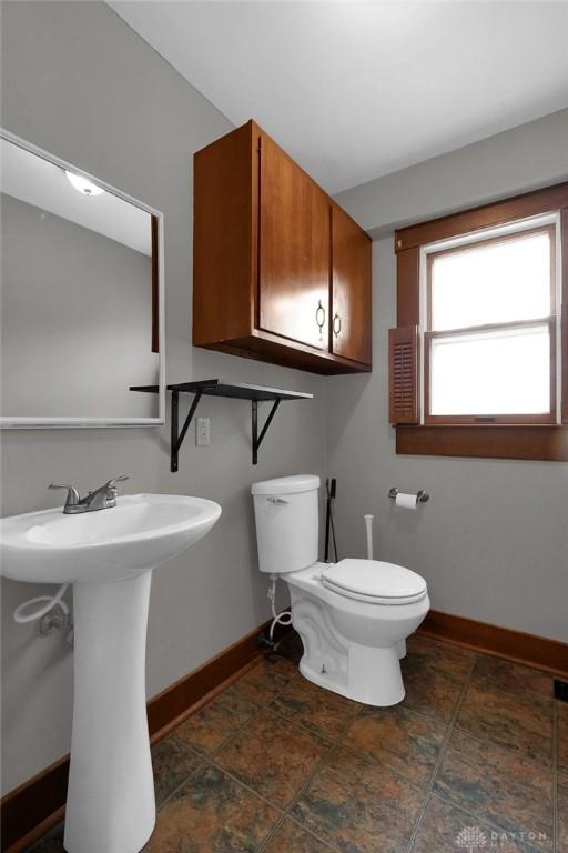 half bathroom with toilet, baseboards, and a sink