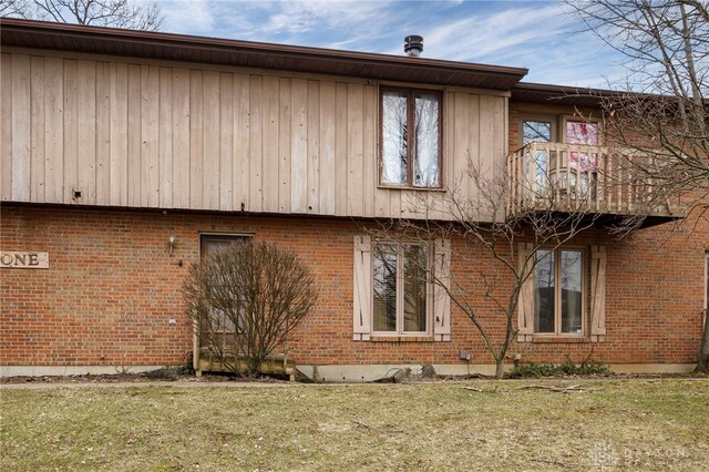 view of side of property with a balcony, a yard, and brick siding