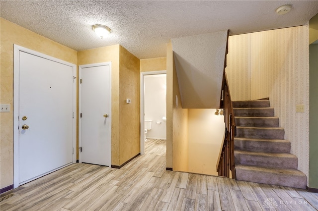 entrance foyer featuring a textured ceiling, stairway, and light wood-style flooring