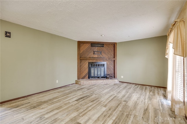 unfurnished living room featuring a fireplace, light wood-style flooring, baseboards, and a textured ceiling