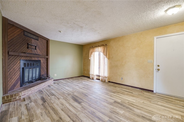 unfurnished living room with a textured ceiling, a fireplace, wood finished floors, and baseboards