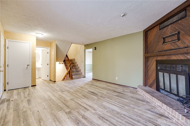 unfurnished living room with a textured ceiling, light wood-style flooring, a fireplace, baseboards, and stairway