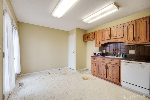 kitchen featuring light floors, dark countertops, brown cabinetry, a sink, and white dishwasher