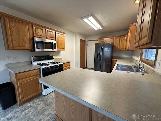 kitchen with range with gas stovetop, stainless steel microwave, a sink, a peninsula, and black fridge