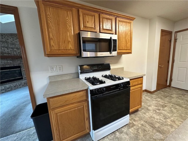 kitchen with light countertops, stainless steel microwave, gas stove, and a brick fireplace