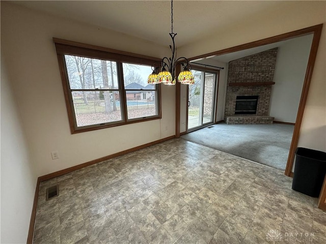 unfurnished dining area with baseboards, visible vents, lofted ceiling, a brick fireplace, and a chandelier