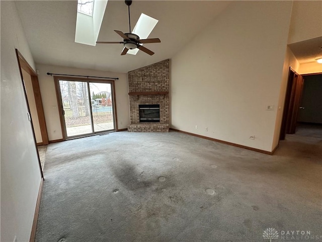 unfurnished living room featuring carpet floors, a skylight, a fireplace, high vaulted ceiling, and baseboards