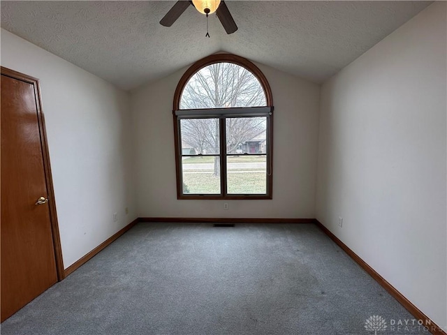 carpeted spare room featuring lofted ceiling, ceiling fan, baseboards, and a textured ceiling