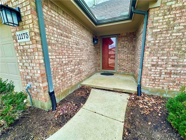 property entrance with a garage, roof with shingles, and brick siding